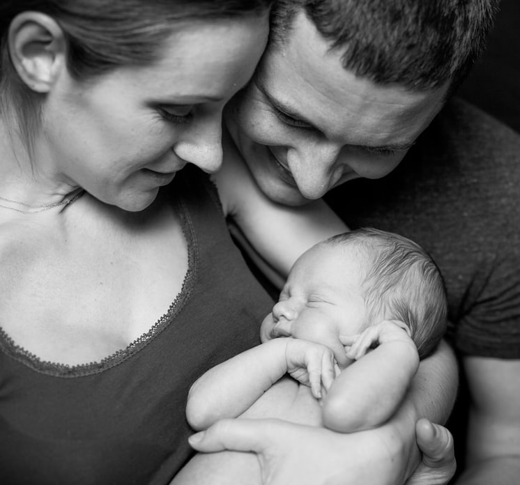 Photo en noir et blanc d'un couple souriant tendrement à leur nouveau-né endormi, symbolisant les soins de la petite enfance et la chaleur familiale dans les Pyrénées Orientales
